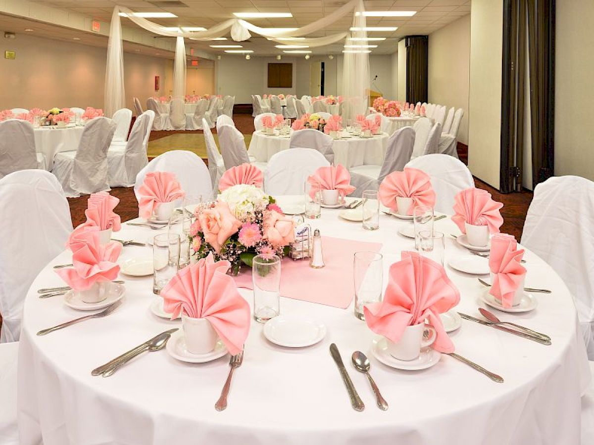 This image shows a banquet hall decorated for an event, with white-clothed tables, pink napkins, and floral centerpieces, set for a formal gathering.