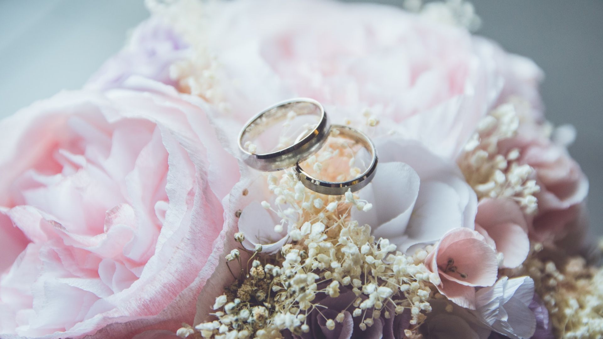 Two wedding rings rest on a bouquet of soft pink and white flowers, symbolizing love and commitment.