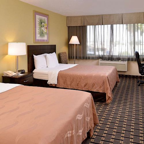 The image shows a hotel room with two beds, a TV, desk, lamps, and a large window with curtains.