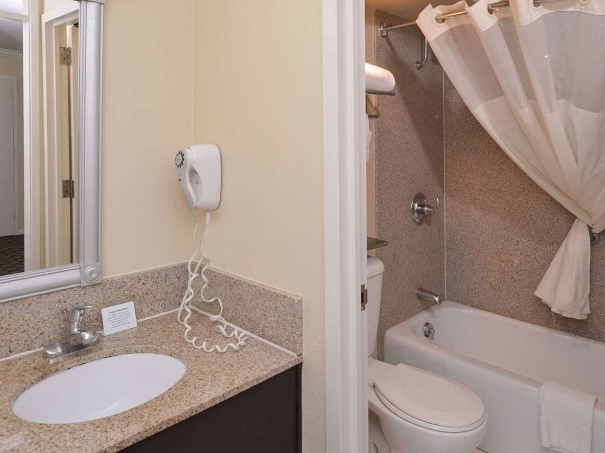 The image shows a bathroom with a sink and mirror, a wall-mounted hairdryer, and a bathtub with a shower curtain.