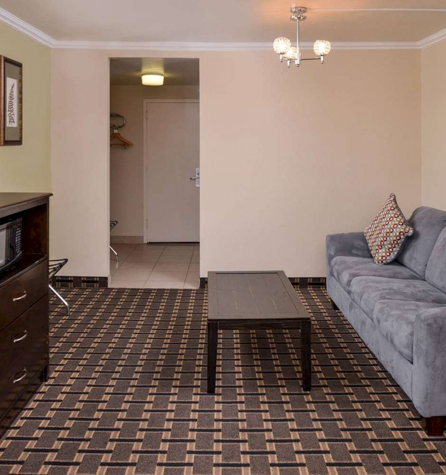 A living room with a patterned carpet, a grey couch, a coffee table, a TV on a stand, framed wall art, and a closet area in the background.