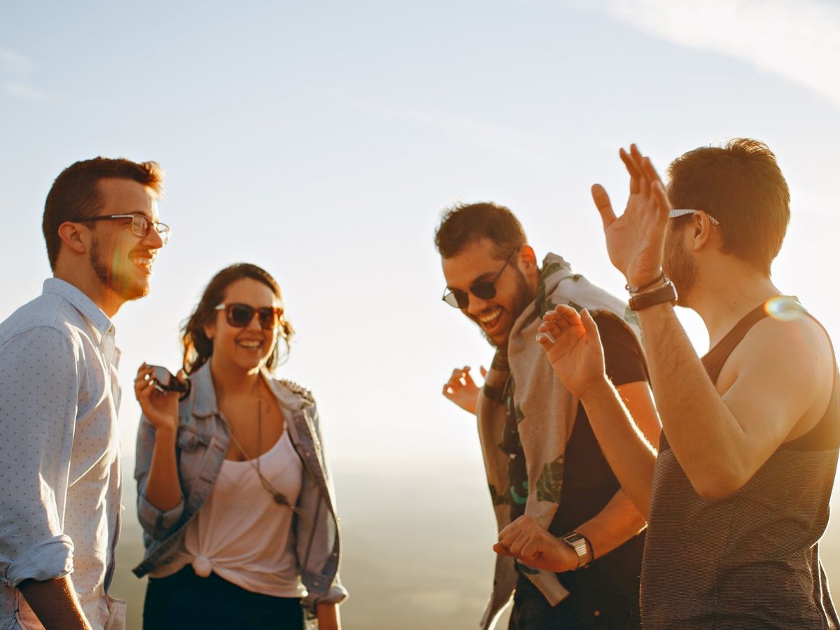 Four adults are outdoors, laughing and chatting. They appear to be enjoying each other's company against a bright, clear sky.