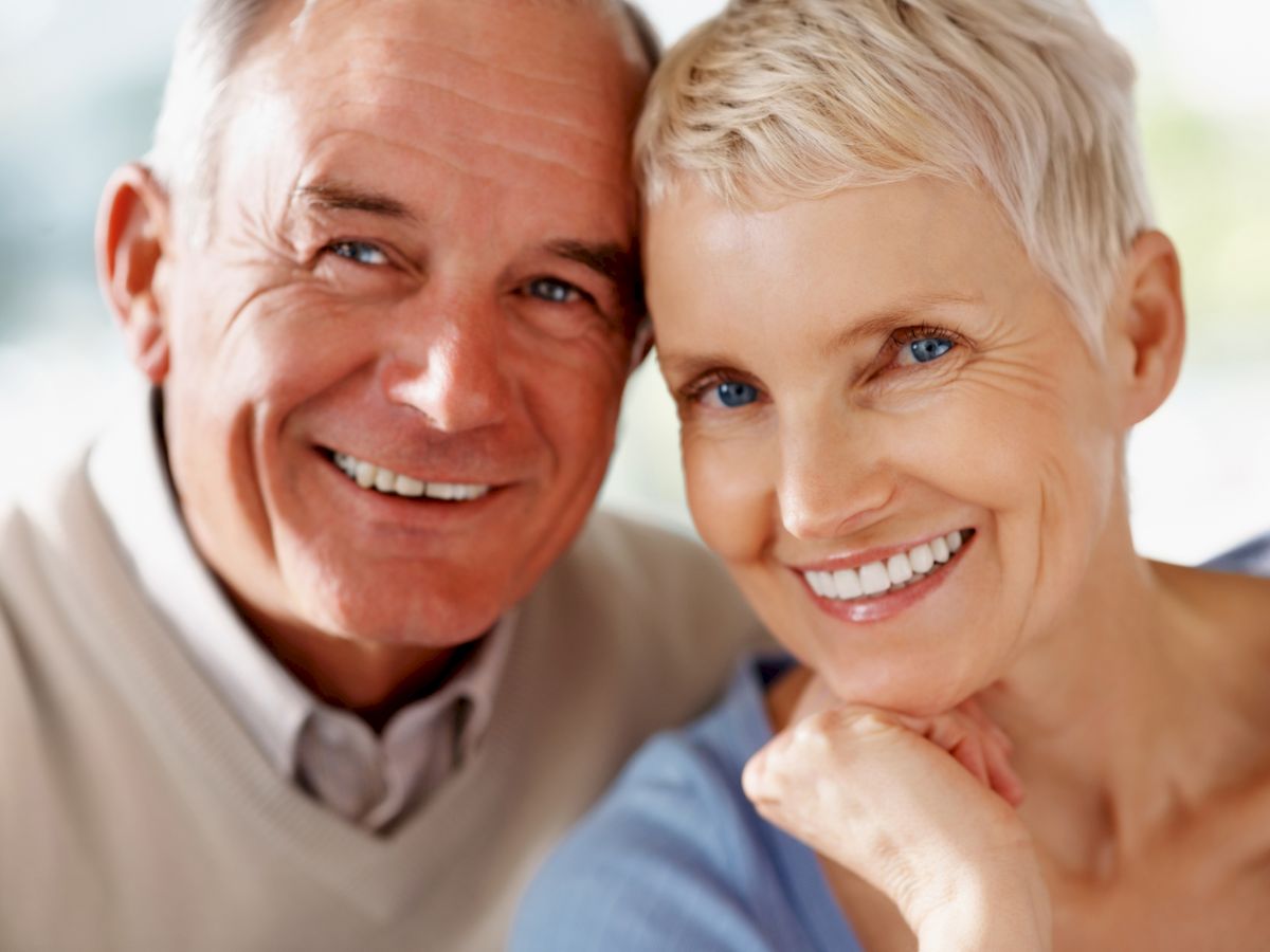 An older man and woman are smiling together in a close-up portrait, with natural light softly illuminating their faces, creating a warm and happy atmosphere.