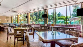 A spacious indoor dining area with tables and chairs, large windows providing a view of a pool and greenery outside.